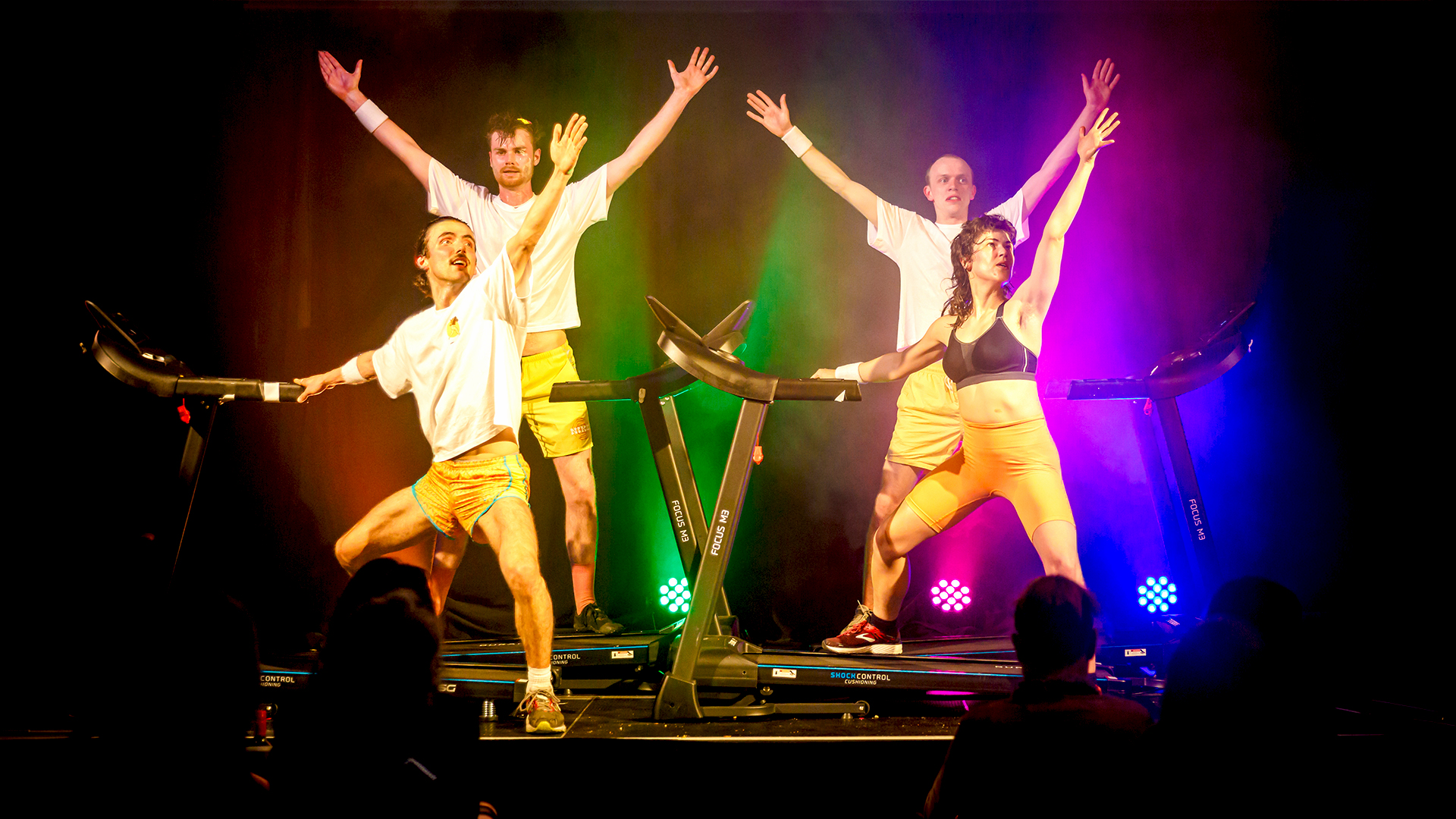 Four performers on four treadmills with arms raised